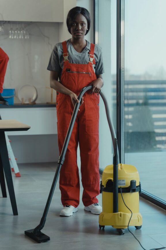 A woman in coveralls using a vacuum cleaner at home, illustrating the choice between DIY cleaning and hiring a professional